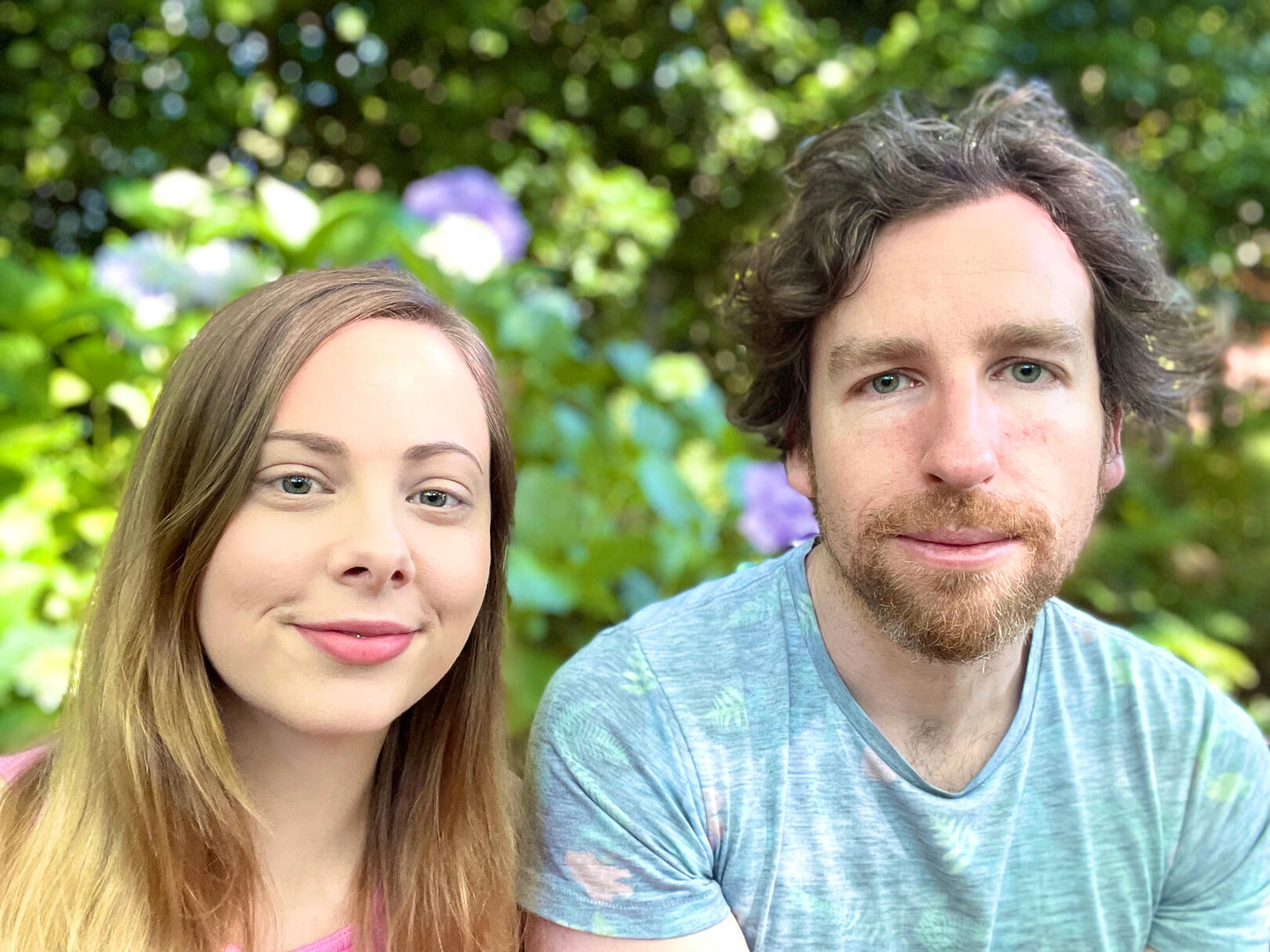 Photo of two people, a woman and a man, sitting side by side with nature behind them