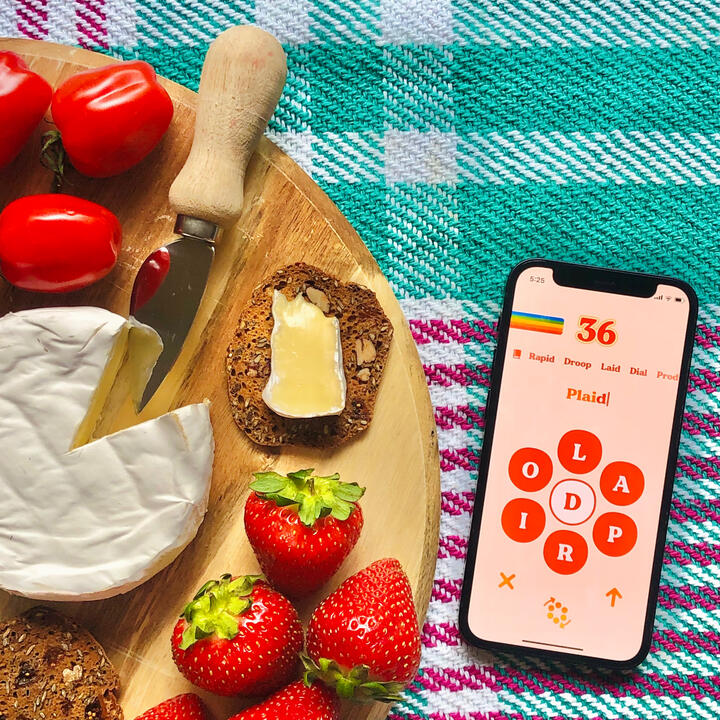 Retrogram game screen displayed on iPhone next to a cheese and fruit board